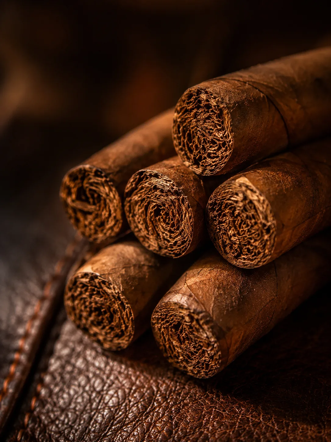 Close-up of hand-rolled cigars stacked on rich brown leather